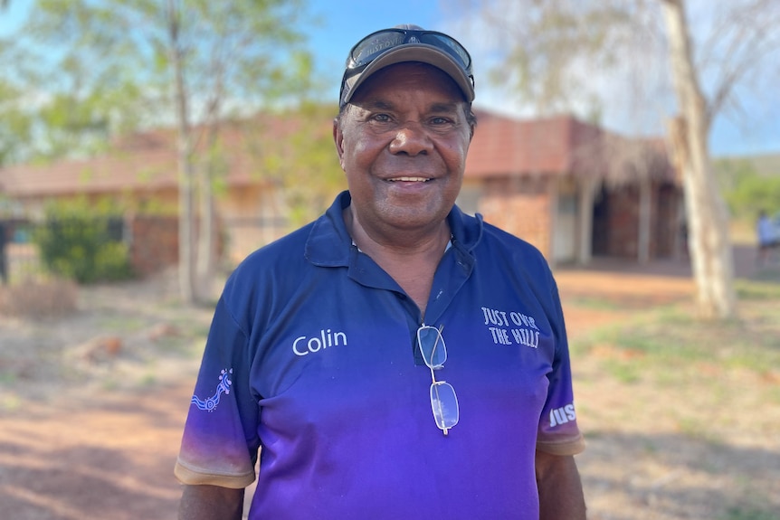 An indigenous man looks into the camera standing outside a community hall