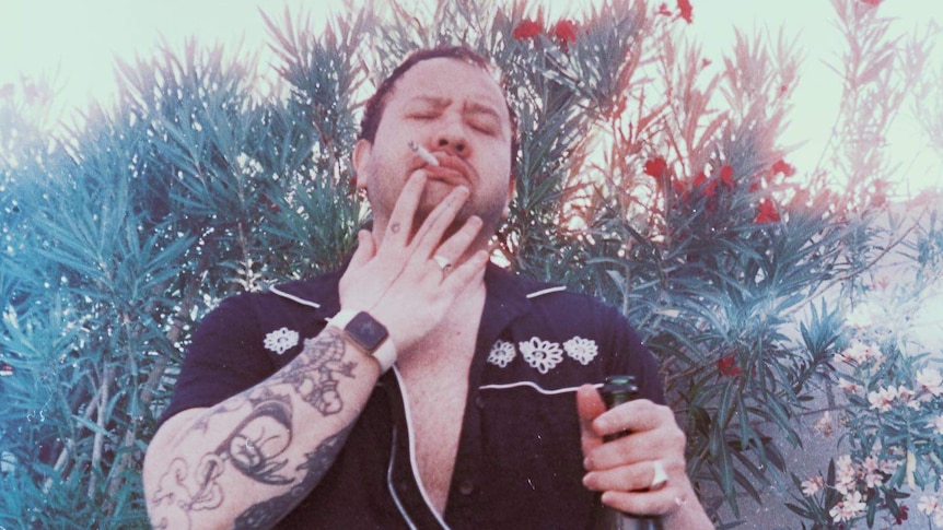 A man smokes a cigarette while holding a bottle of wine with his eyes closed
