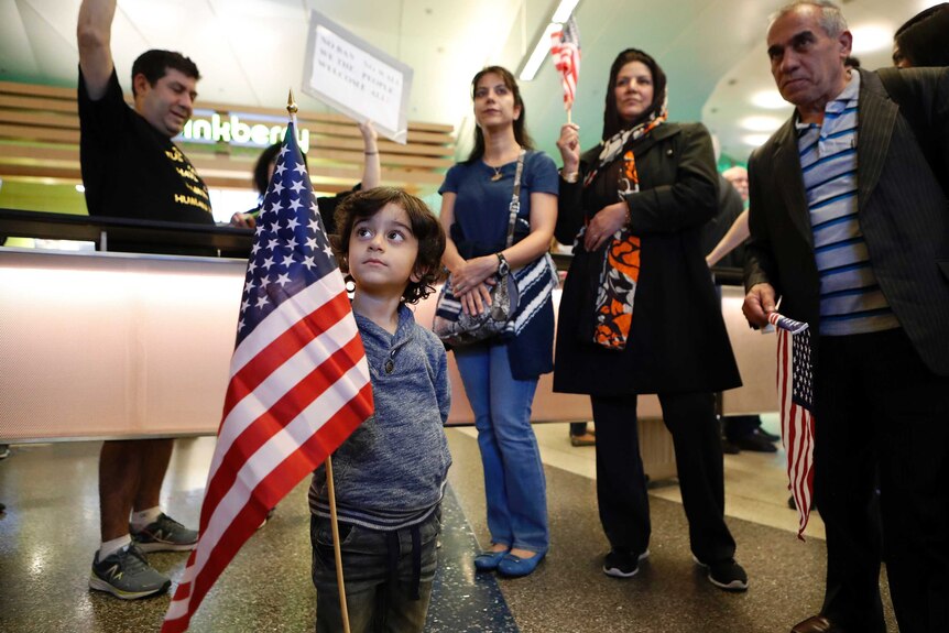 Three-year-old Shayan Ara holds an American flag surrounded by people at LAX