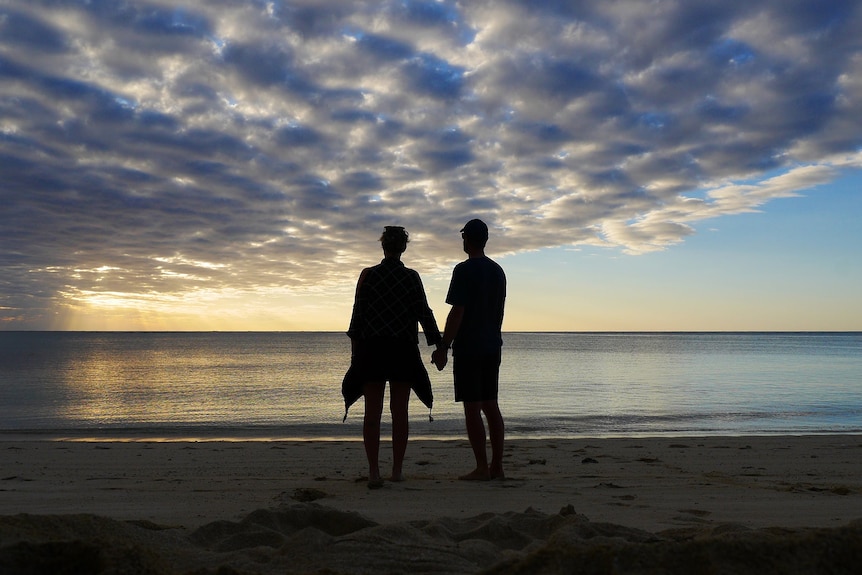 Backlit woman and man standing on a beach.