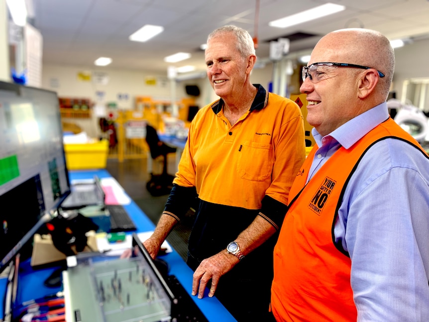 AMP Control CEO Rod Henderson (foreground) looks at some of the firm's equipment with a staff member.