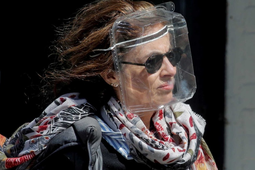 A woman wears a plastic food container for protection with her scarf flowing and sunglasses.