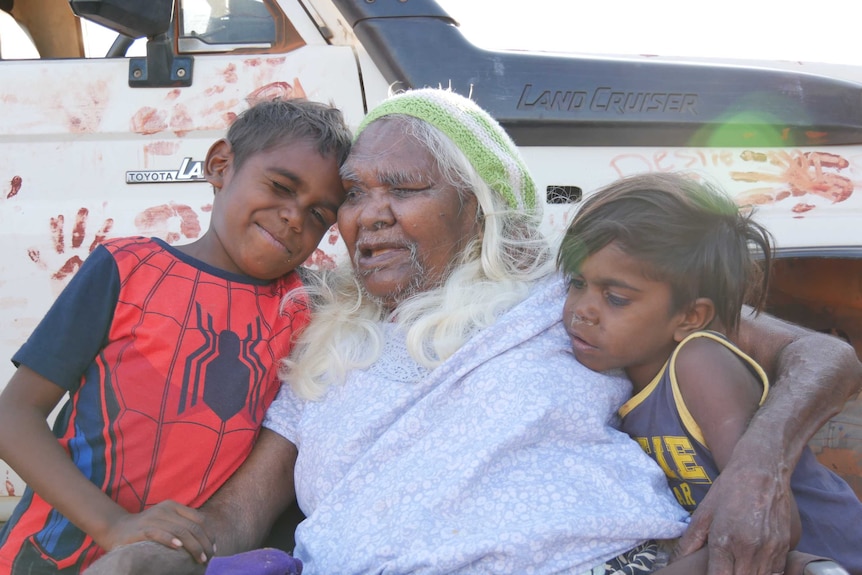 An elderly woman cuddles her two grandsons.