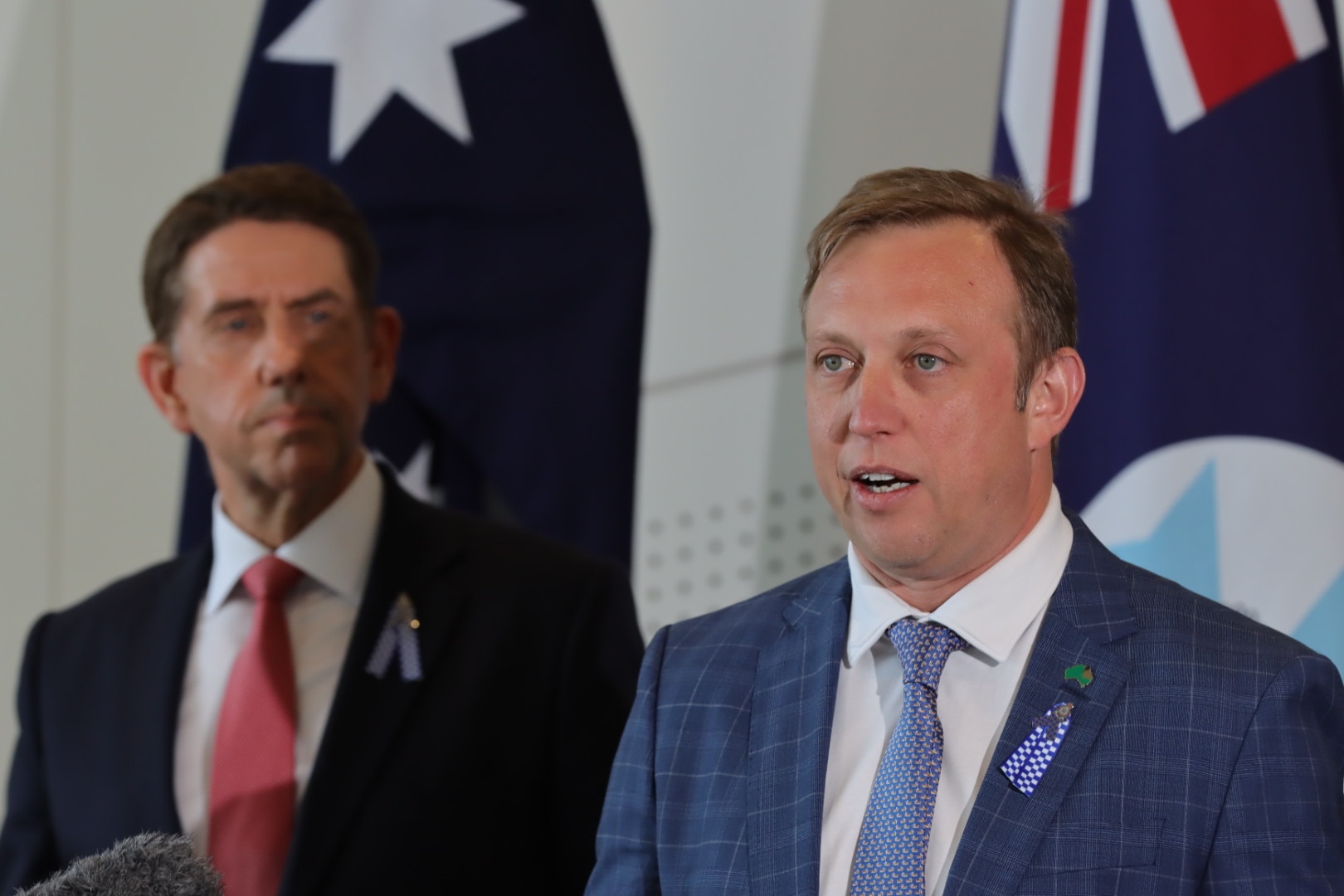 A man in a blue suit and tie stands next to a man in a black suit and red tie.