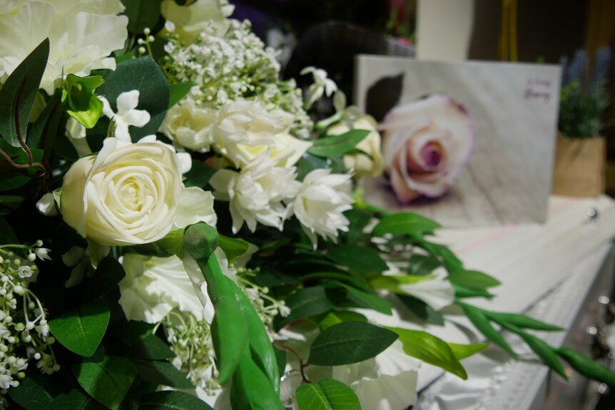 A bouquet of white roses on top of a coffin.