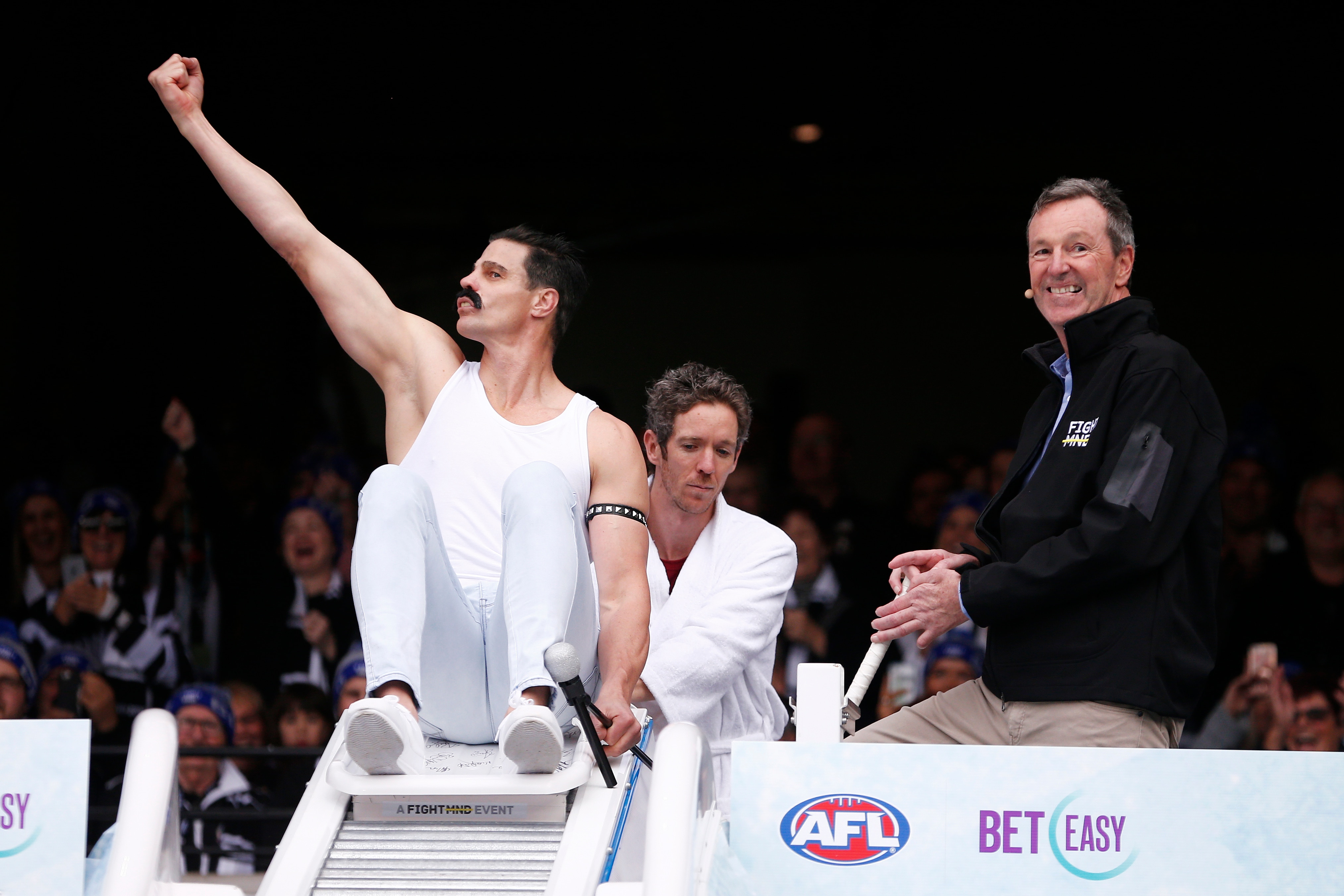Um jogador de futebol aposentado da AFL vestido como Freddie Mercury se prepara para entrar em um banho de gelo, enquanto Neale Daniher sorri.