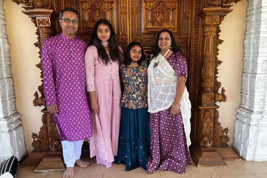 Family of four in traditional indian outfits standing against a golden door