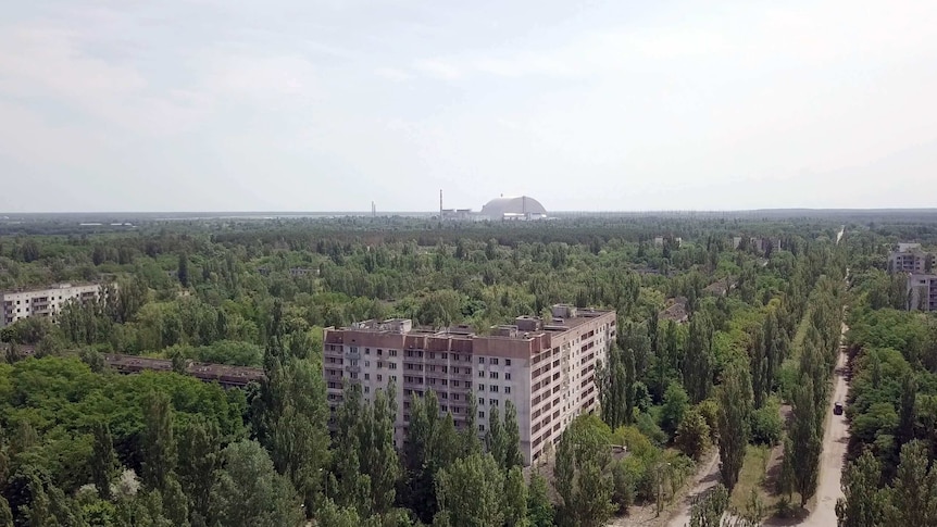 A drone shot showing the abandoned city of Pripyat with the Chernobyl reactor in the background.