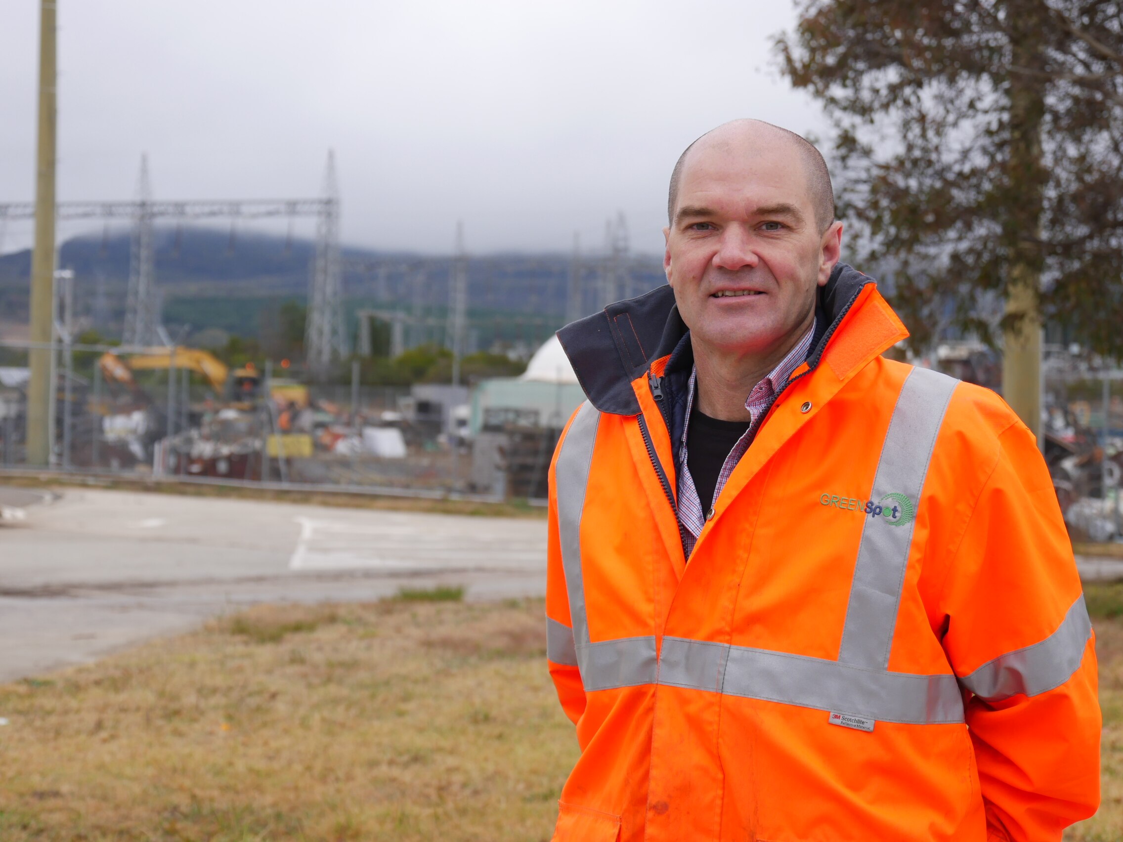 A man wearing a high-visibility jacket stands outside on a foggy day.