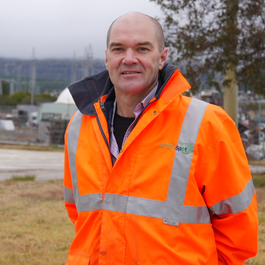 A man wearing a high-visibility jacket stands outside on a foggy day.