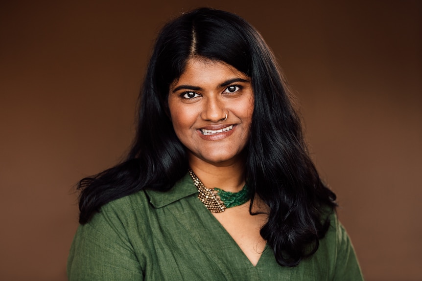 Head and shoulders image of a woman in a green shirt smiling in front of a red backdrop.