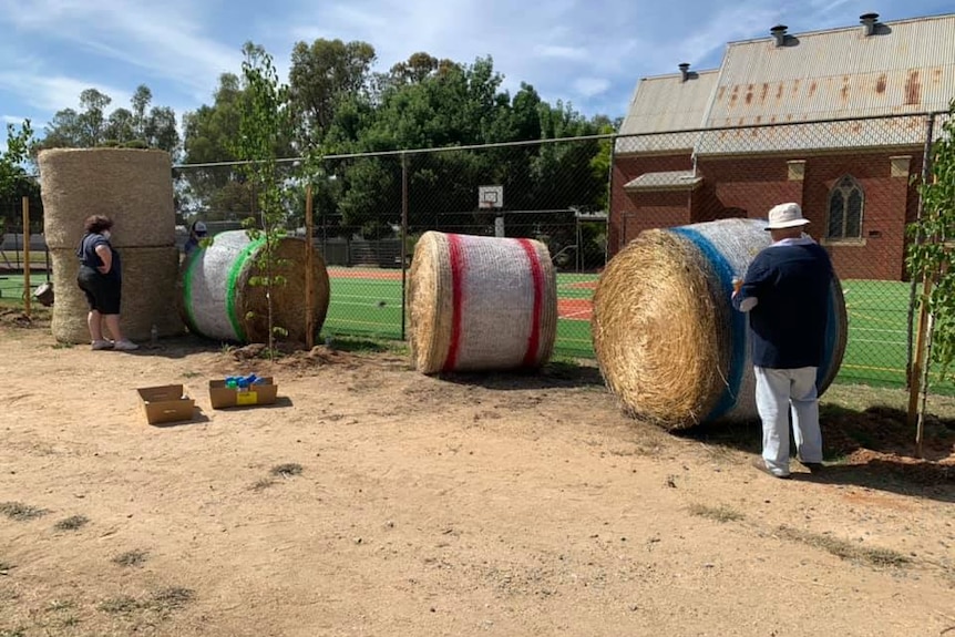 five large round hay bales, three painted white with coloured striped.
