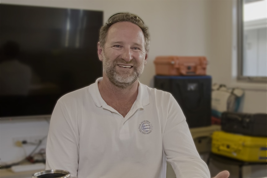 Dr Simon Allen, wearing a white polo shirt in an office smiling at the camera