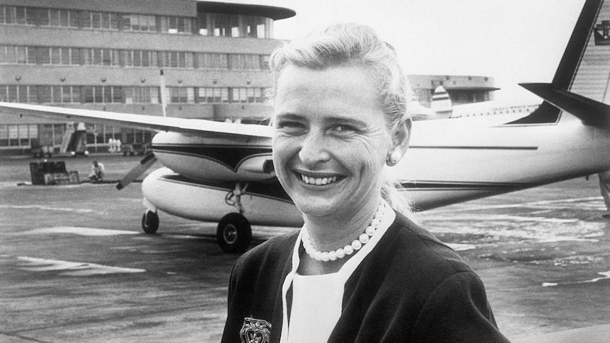 Blon attractive woman standing in front of a small plane in an airport