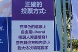 A poster in purple and white is attached to a fence next to an official AEC polling poster.