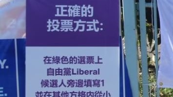 A poster in purple and white is attached to a fence next to an official AEC polling poster.