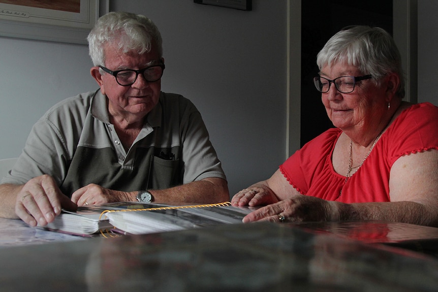 Husband and wife sitting around the dinner table together while looking at old photographs.