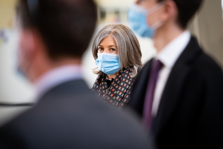 A woman wearing a mask looking aside with people in the foreground