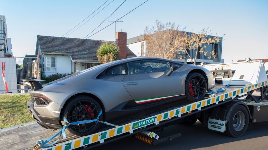 A silver sportscar is loaded onto a tow truck.