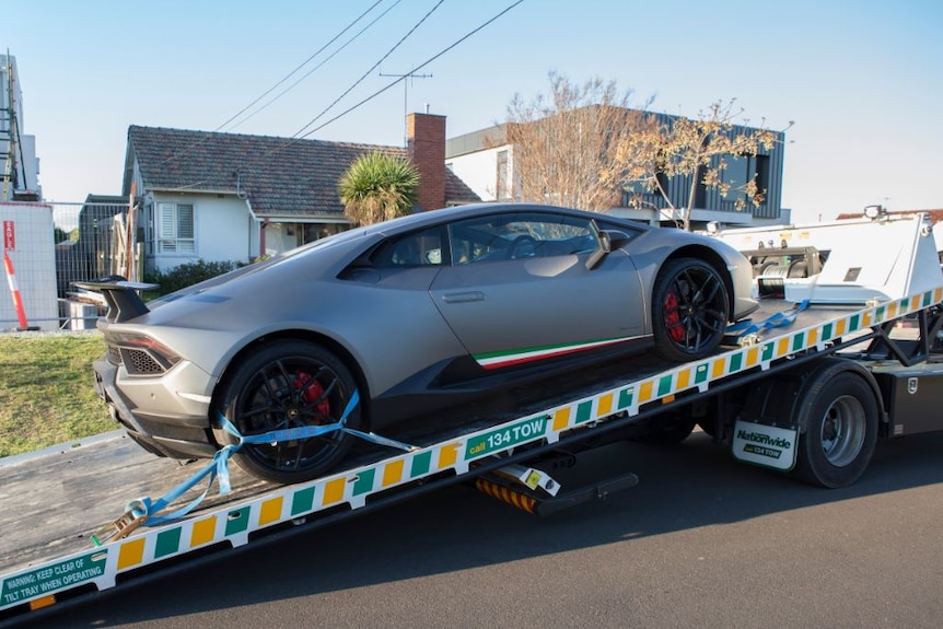 A silver sportscar is loaded onto a tow truck.