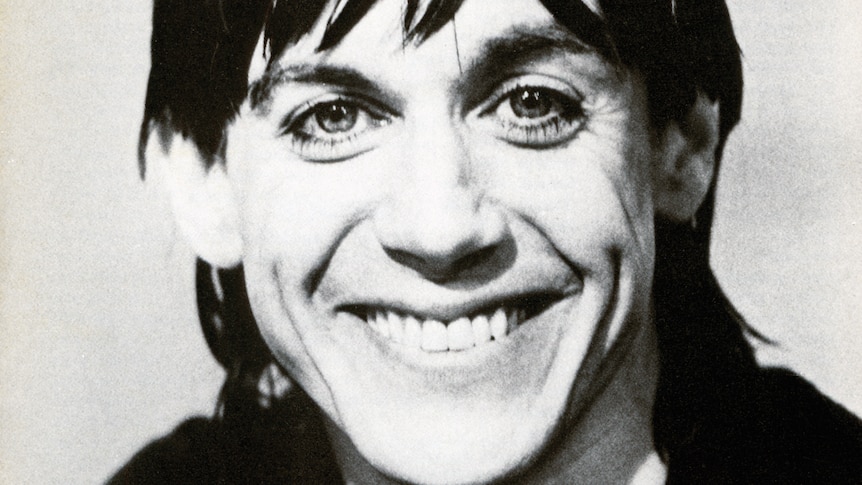 Close-up black and white photo of a grinning Iggy Pop