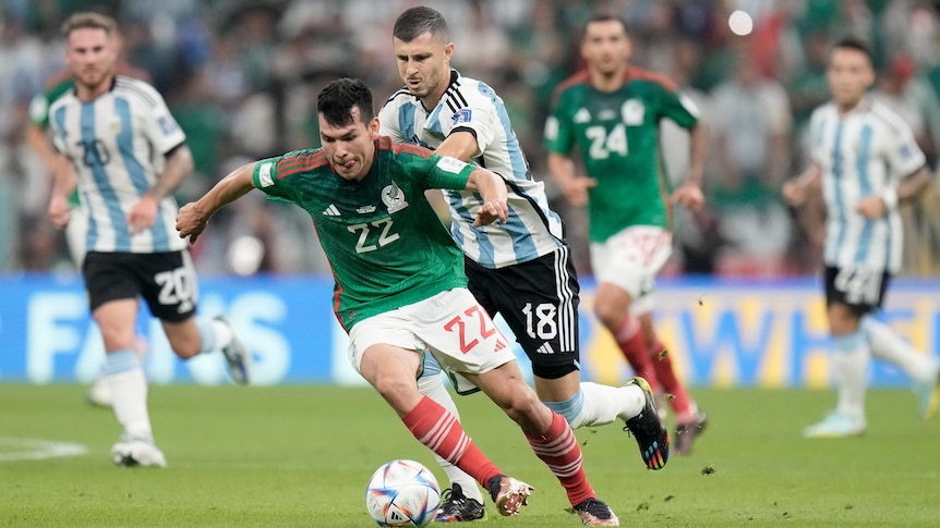 A Mexican player puts his head down, and runs with the ball as an Argentinian defender tries to stop him.