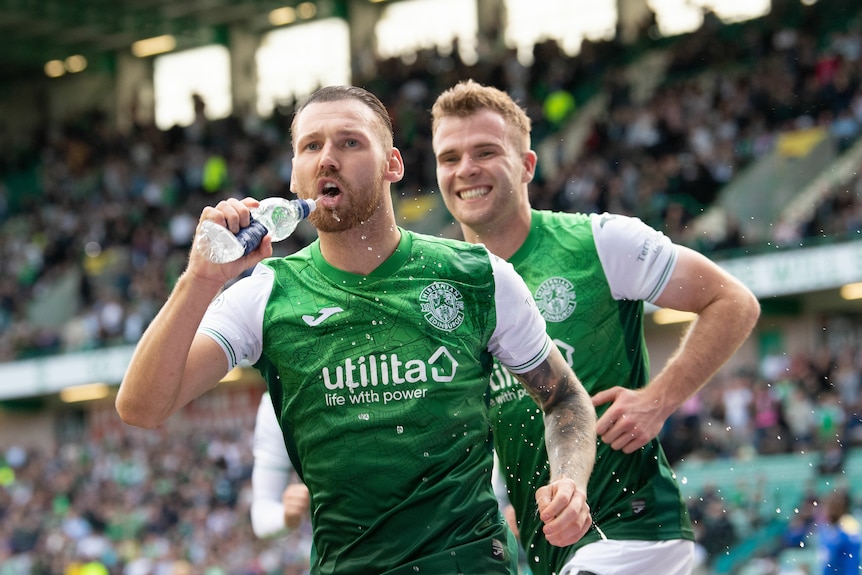Martin Boyle squirts water into his mouth from a bottle as a smiling teammate runs behind him