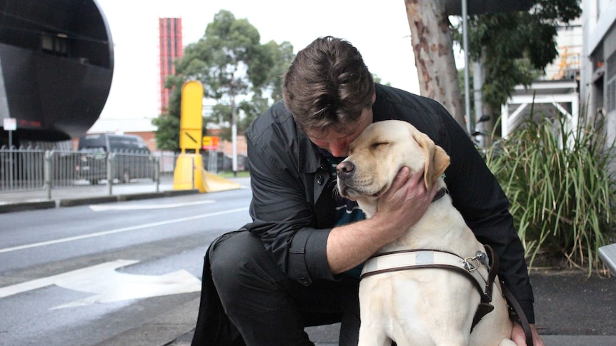 Disability access advocate David Foran kneels with his guide dog, Oliver, at a tram stop in Southbank