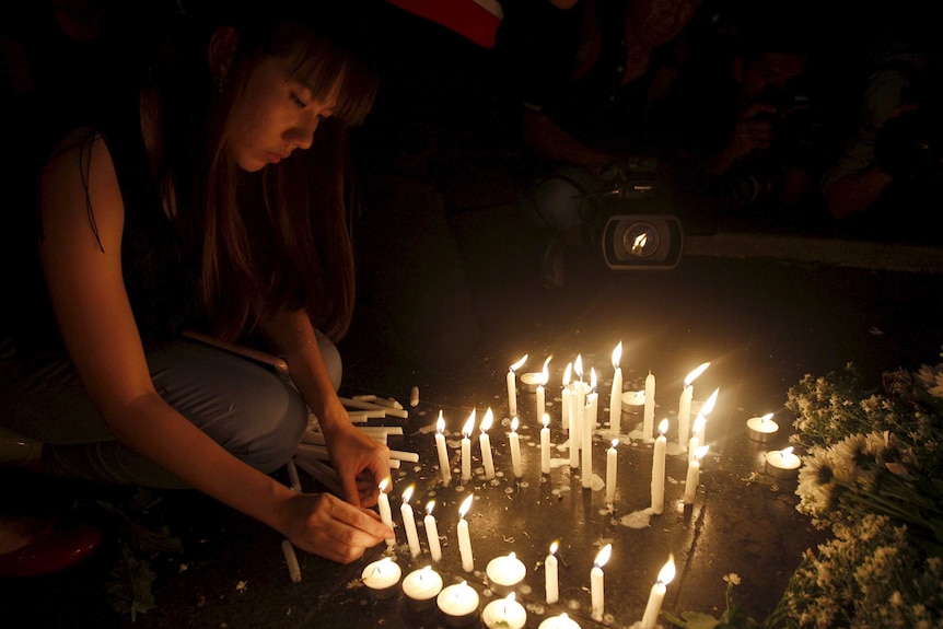 A woman lights a candle at a memorial in Bangkok