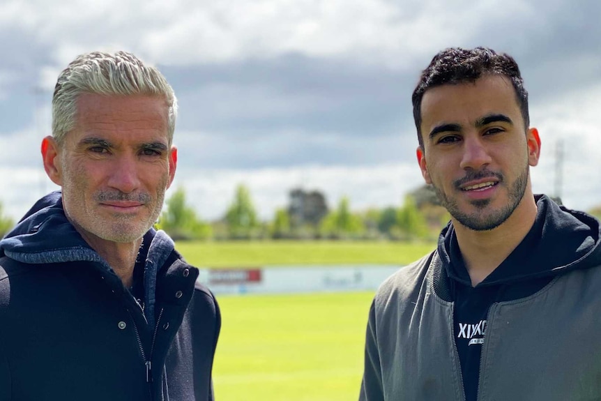 Two men stand next to each other on a football pitch