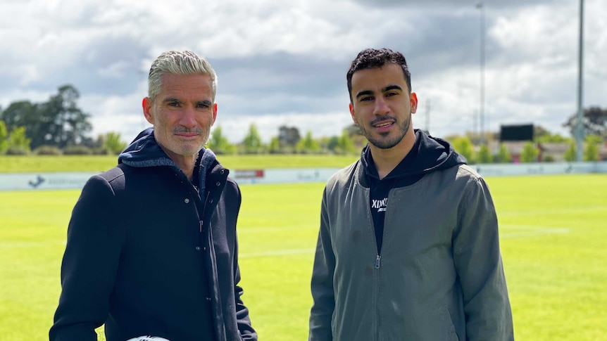 Two men stand next to each other on a football pitch