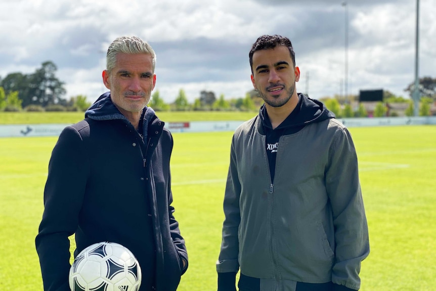 Two men stand next to each other on a football pitch