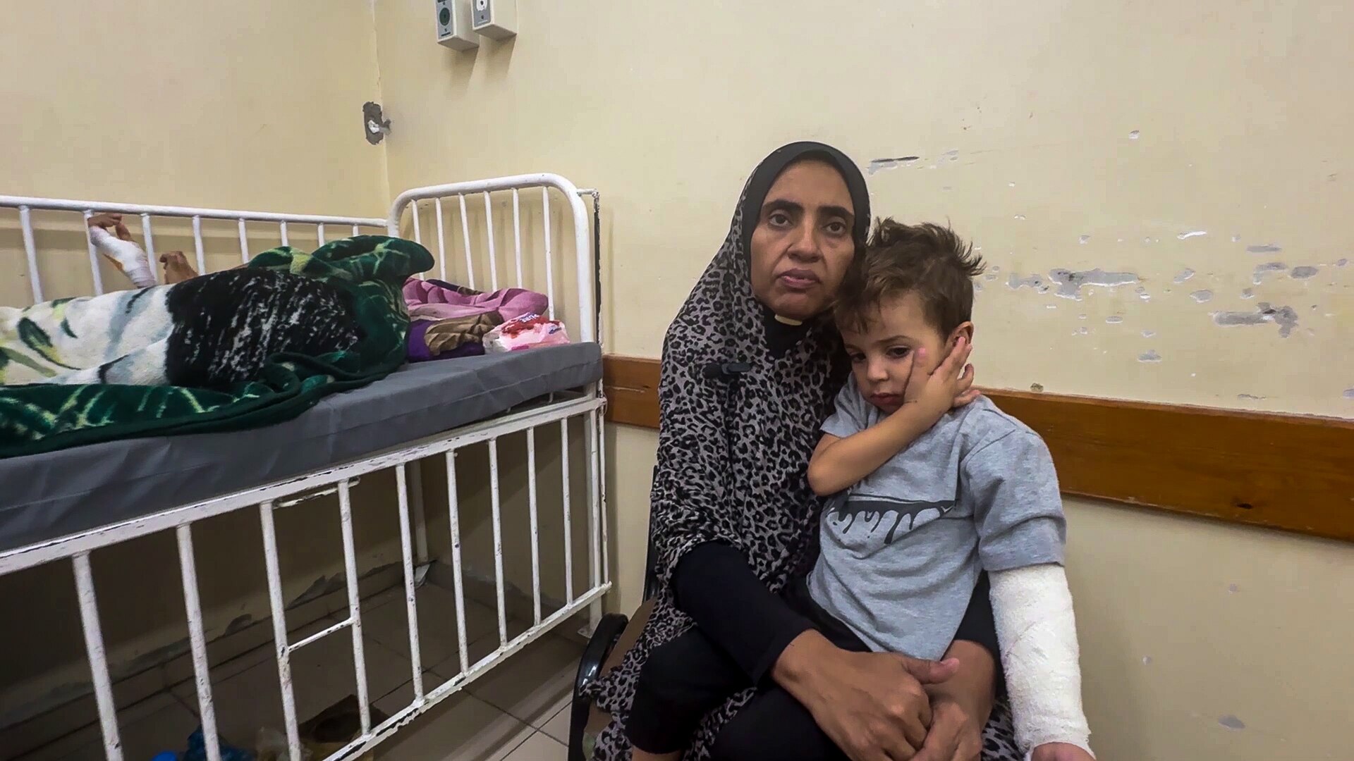 Saana Redwan sits in a hospital room hugging an injured boy who is perched on her leg.