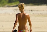 A topless woman walks along a beach