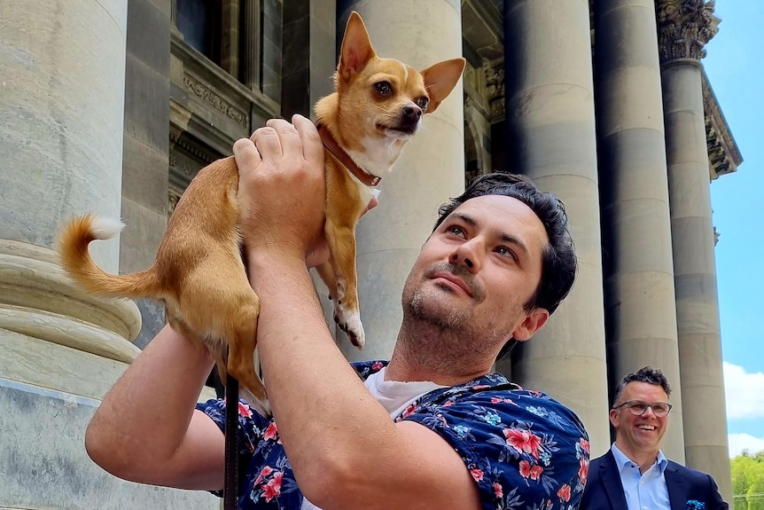 A man holding a small dog up in the air.