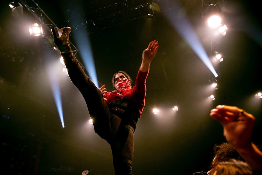 A vogue dancer wearing a red scarf over her mouth high kicks the air onstage at Sissy Ball 2019.