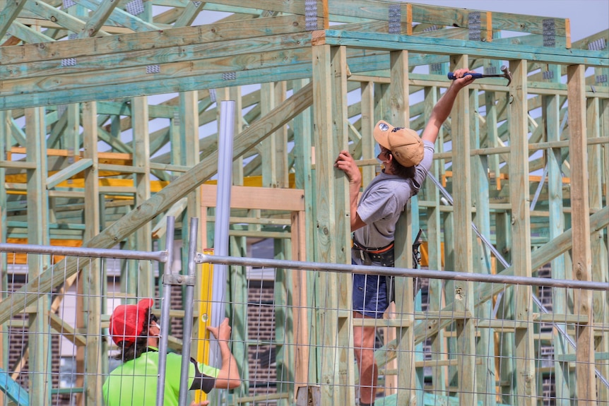 Two workers on a construction site, hammering in a frame for a house.