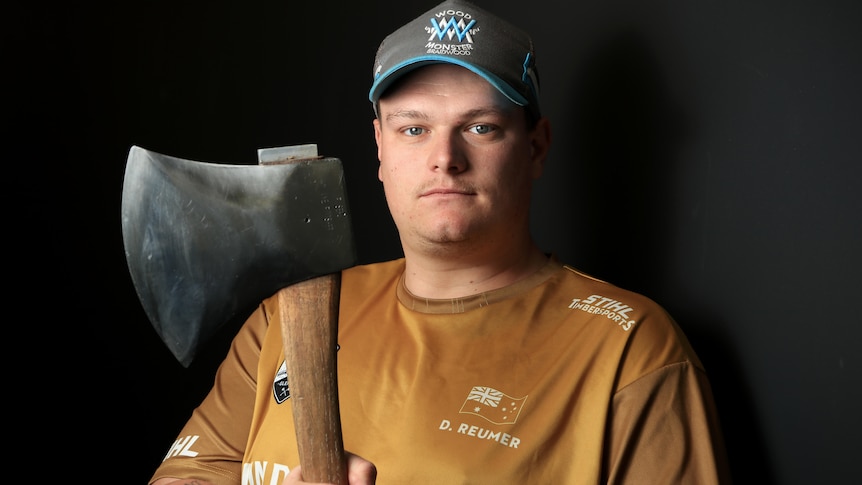 A young man in a cap stands holding an axe.