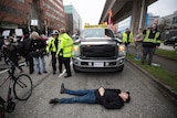 A counter protester lies on the road in front of a truck