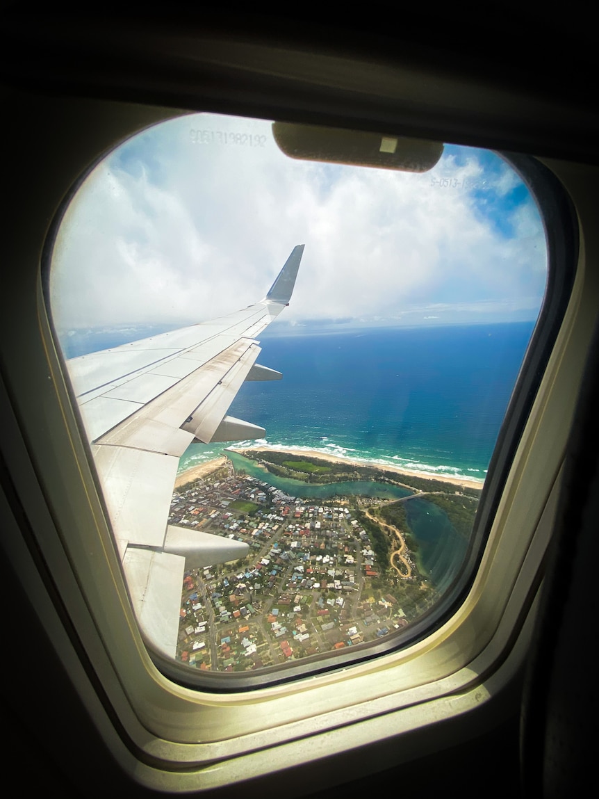 A view of a coastline out the window of a plane with a wing in shot