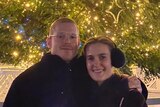 A young man and woman pose for a photo in front of a Christmas tree