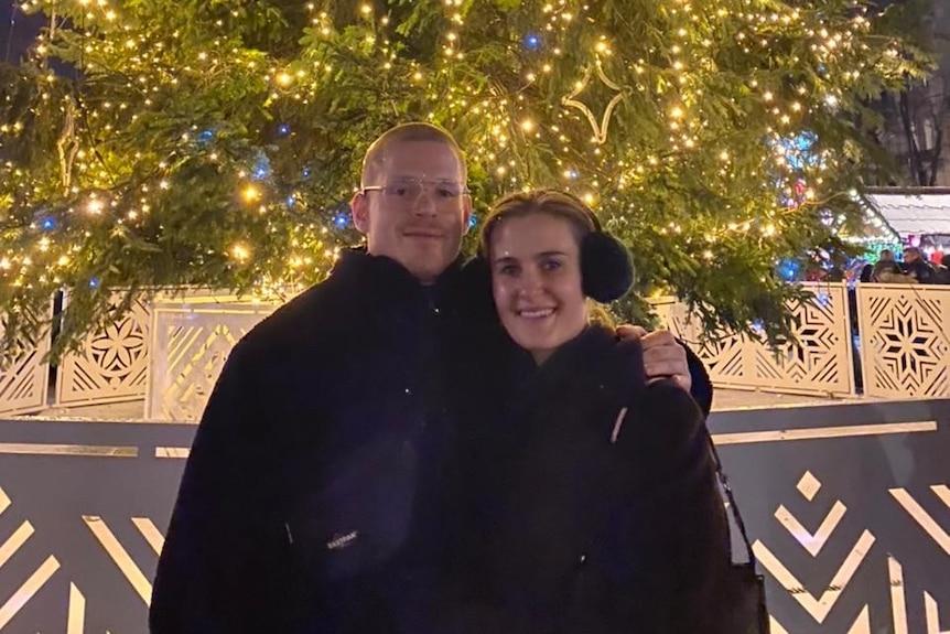 A young man and woman pose for a photo in front of a Christmas tree