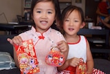 Young girls smile and hold up red cards and packets decorated with Lunar New Year symbols.