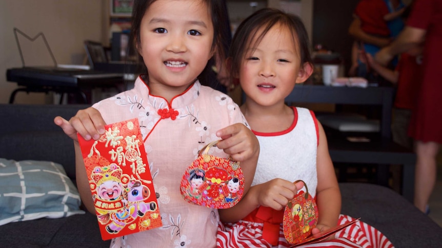 Young girls smile and hold up red cards and packets decorated with Lunar New Year symbols.