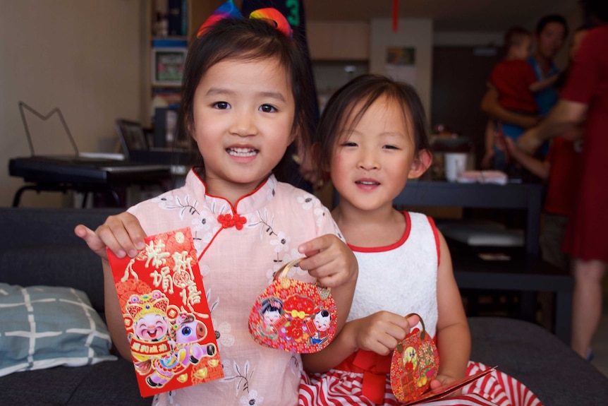 Young girls smile and hold up red cards and packets decorated with Lunar New Year symbols.