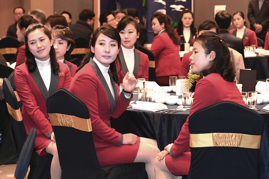 North Korean women wearing black-trimmed red blazers sit at banquet tables.