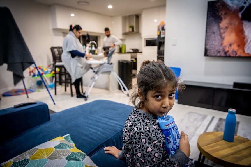 A young girl sits on a couch and sips from a drink in a living room