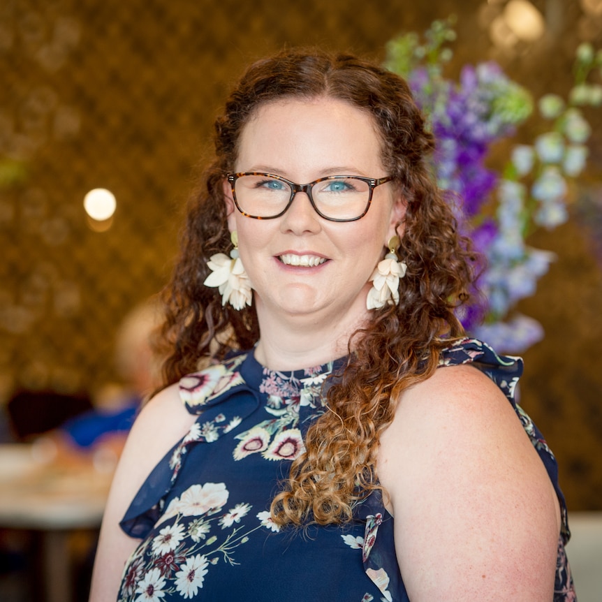 A profile image of a woman with long, curly hair and glasses, standing in a restaurant.