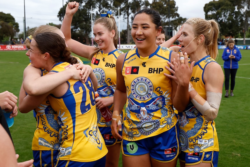 West Coast Eagles players smile and embrace on the field after an AFLW win.