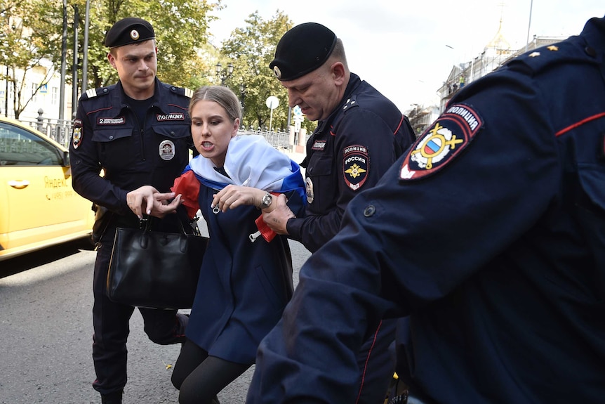 Police officers drag a woman as she speaks angrily.